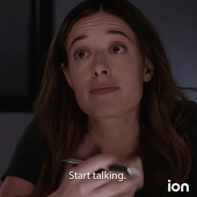A woman with long brown hair raises her eyebrows and speaks in a dim room, captioned 'Start talking.'