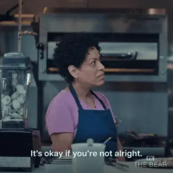 What+Is+Going+On+GIF+by+The+Bear.gif A woman in an apron in a kitchen looks aside, captioned 'It's okay if you're not alright.'