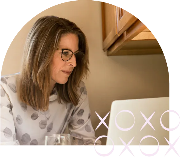 Image-10.png Woman wearing glasses working on a laptop at home, with decorative X and O elements in the corner.