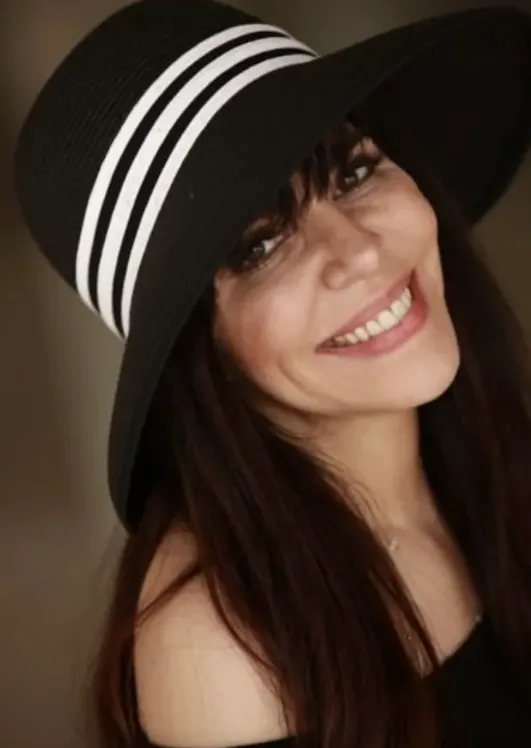 Woman smiling and wearing a black hat with white stripes.