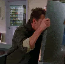 Frustrated+Head+GIF.gif A man in a green jacket strains to push against a large tilted mirror in an office break room while a colleague watches.