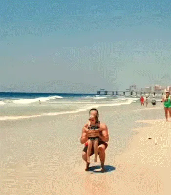A man tosses a young girl into the air and catches her on a sunny beach.