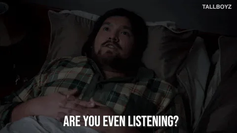 A man in a plaid shirt lies in bed with his hand on his chest and says 'Are you even listening?'