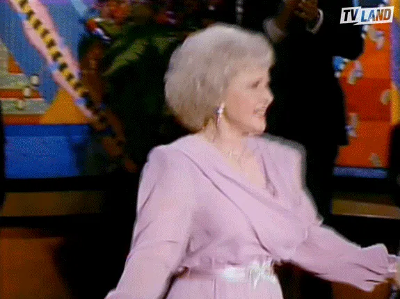 An older woman in a pink dress dances energetically on a colorful stage.