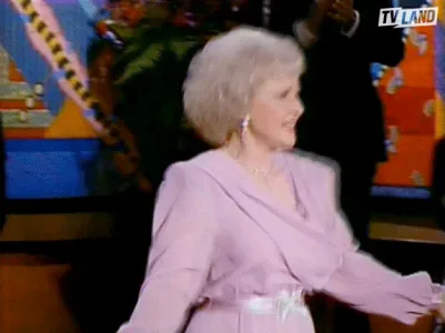 Golden+Girls+Dancing+GIF+by+TV+Land.gif An older woman in a pink dress dances energetically on a colorful stage.