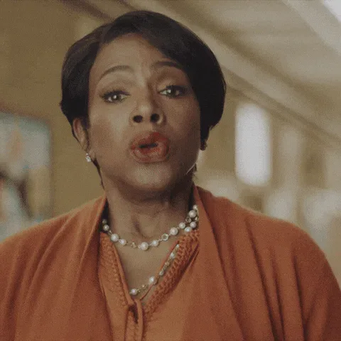 Deep+Breath+Smile+GIF+by+ABC+Network+(1).gif A woman with short dark hair in an orange cardigan closes her eyes, then opens them smiling.