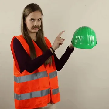 Head+Helmet+GIF+by+Nový+start.gif A woman in an orange vest and fake mustache points at a green hard hat, then facepalms.