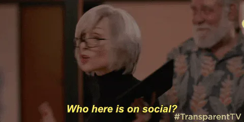 A woman with glasses holds up a tablet and says 'Who here is on social?' as a man watches.