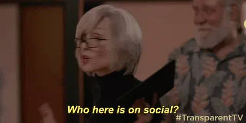 Who+Here+Is+On+Social+Season+3+GIF+by+Transparent.gif A woman with glasses holds up a tablet and says 'Who here is on social?' as a man watches.