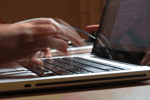 Close-up of a pair of hands typing quickly on a laptop keyboard.