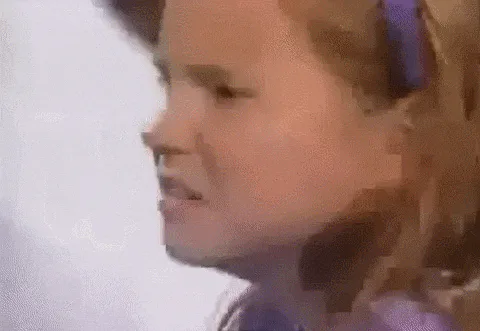 A young girl with a headband makes a scrunched, unimpressed face in a grainy close-up video.