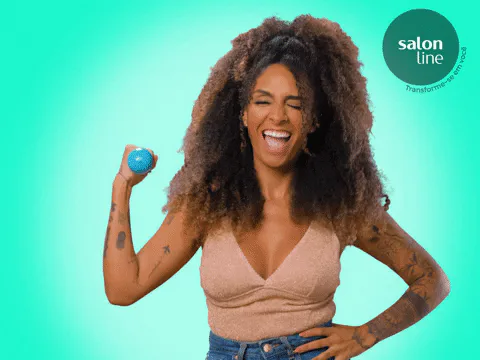 A woman laughs and flexes her bicep while holding a small blue hand weight.