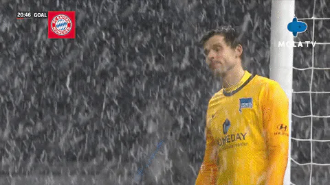 A soccer goalkeeper stands in falling snow as a blue MOLA TV logo animates across the screen near his face.