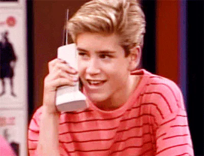 A young man on a retro brick-sized phone smiles and laughs while chatting.