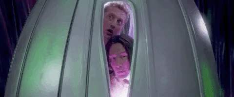 Two people peer wide-eyed through the window of a metal pod, and the word 'Whoa!' appears.
