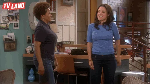 Two women laugh and dance beside a kitchen table.