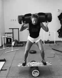 Team+Usa+Sport+GIF+by+U.S.+Ski+&+Snowboard+Team.gif A woman in gym gear balances on a wobble board while carrying a heavy sandbag across her shoulders.