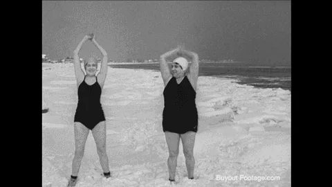 ea0778a2-e4e7-f761-3267-bc65a3ed49db.gif Archival black and white footage shows two women in old-fashioned swimsuits stretching on a snowy beach.