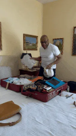 Leaving+See+Ya+GIF+by+Robert+E+Blackmon.gif A bald man tosses a folded white item into an open suitcase on a bed in a yellow room.