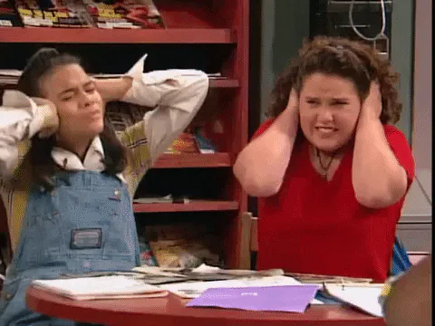 Two young women at a desk covering their ears and wincing at a loud noise.