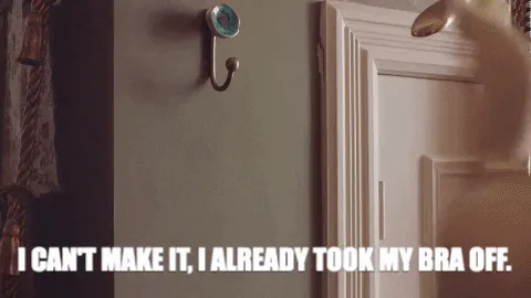 A hand hangs a bra on a wall hook as text reads 'I can't make it, I already took my bra off.'