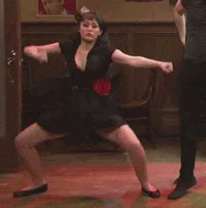 A woman in a black dress with a red rose at her waist dances energetically in a wood paneled room.