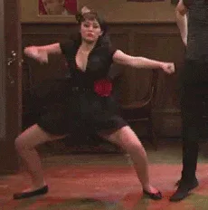 Dance+Dancing+GIF.gif A woman in a black dress with a red rose at her waist dances energetically in a wood paneled room.