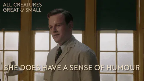 Channel+5+Lol+GIF+by+All+Creatures+Great+And+Small.gif A young man in a beige suit smiles by a window and says 'She does have a sense of humour.'