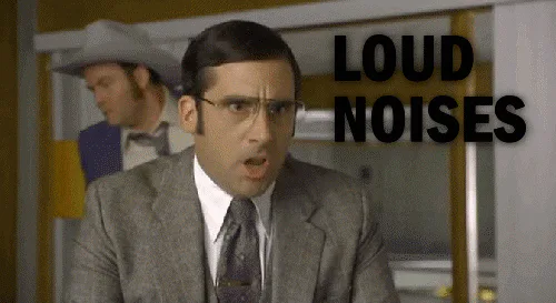 A man in a suit and glasses yells with his mouth wide open as the caption reads 'Loud noises.'