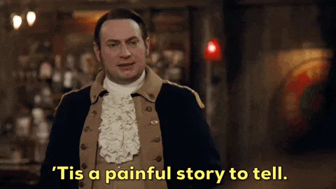 A man in a colonial-era coat raises his hands and says 'Tis a painful story to tell.'
