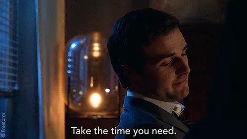 A man in a suit stands beside a glowing lamp at night and says 'Take the time you need.'