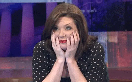 A woman rests her chin on both hands, eyes wide with nervous anticipation.