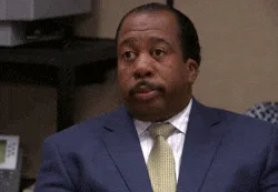 A man in a navy suit and gold tie gives a deadpan look before slowly closing his eyes.