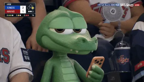 Awkward+Live+Sports+GIF.gif A green cartoon crocodile toy holds a phone while sitting among baseball fans at a live game broadcast.