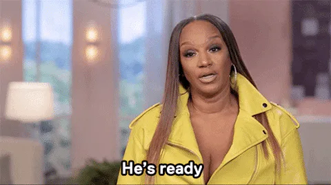 A woman in a yellow leather jacket speaks emphatically, captioned 'He's ready.'