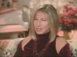 A blonde woman in a maroon top talks in front of flowers and says 'It's absurd!'