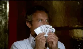cards+juking+GIF.gif A man in a white robe peers over a fanned hand of playing cards held up to his face.