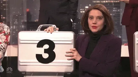 deal+or+no+deal+snl+GIF+by+Saturday+Night+Live.gif A woman in a purple blazer smiles while holding a silver briefcase marked with a large number 3.