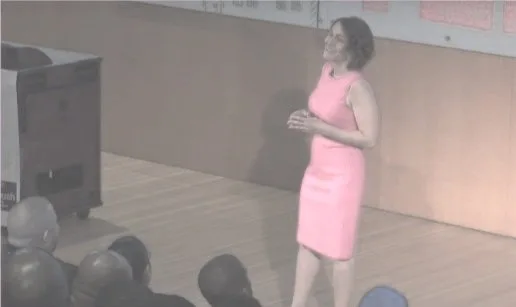 Picture1.jpg A woman in a pink dress speaking on stage to an audience