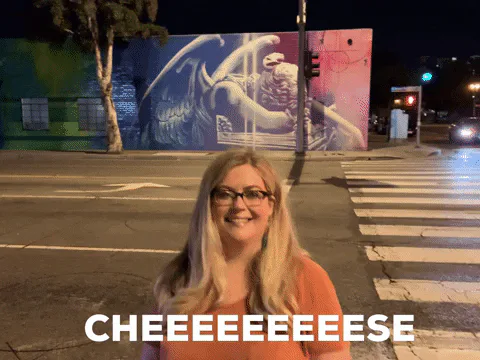 A woman in glasses smiles for a photo at a night time street crossing as the caption reads 'Cheeeeeeeeese.'