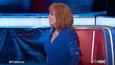 Boo+Thumbs+Down+GIF+by+The+Voice.gif A red-haired woman in a blue dress gestures animatedly in front of a red chair on The Voice.