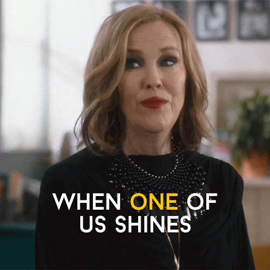 A woman with wavy hair says 'When one of us shines' then 'all of us shine' in on-screen text.