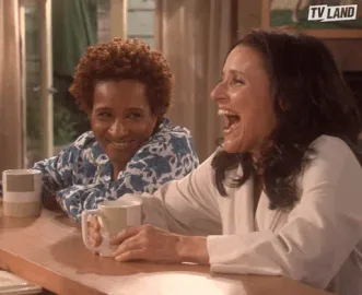 Oct 8 i.2 Two women laugh together at a kitchen counter, each holding a mug.