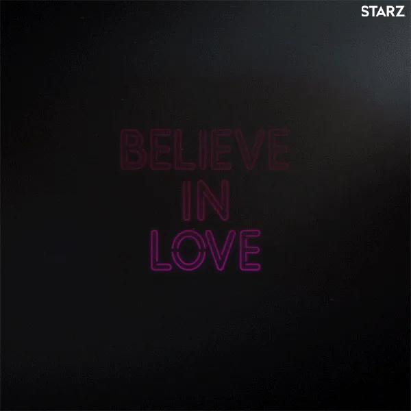 Glowing pink neon letters spelling 'Believe in Love' brighten against a dark background.