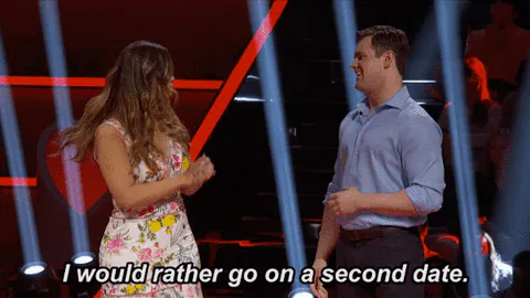 A woman in a floral dress gestures toward a man on a lit stage as text reads 'I would rather go on a second date.'