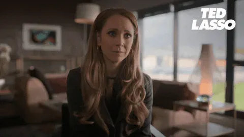 42a3b6bf-50d5-8f7f-32e7-86a08bd718d1.gif A woman with long red hair winces, then smiles while saying 'You've got this!' in a cozy, dim living room.