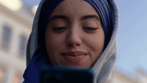 A woman wearing a blue headscarf smiles down at her phone.
