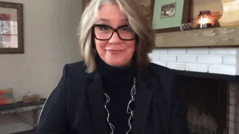 A woman in glasses holds two green pea toys near her face as on-screen text spells out 'Pretty peas!'