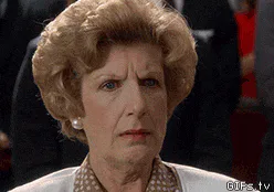 A woman with curly reddish blond hair purses her lips in a disapproving close-up.