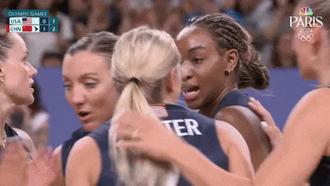 Two teammates in navy USA jerseys embrace and celebrate with teammates during a Paris 2024 Olympic volleyball match against China.